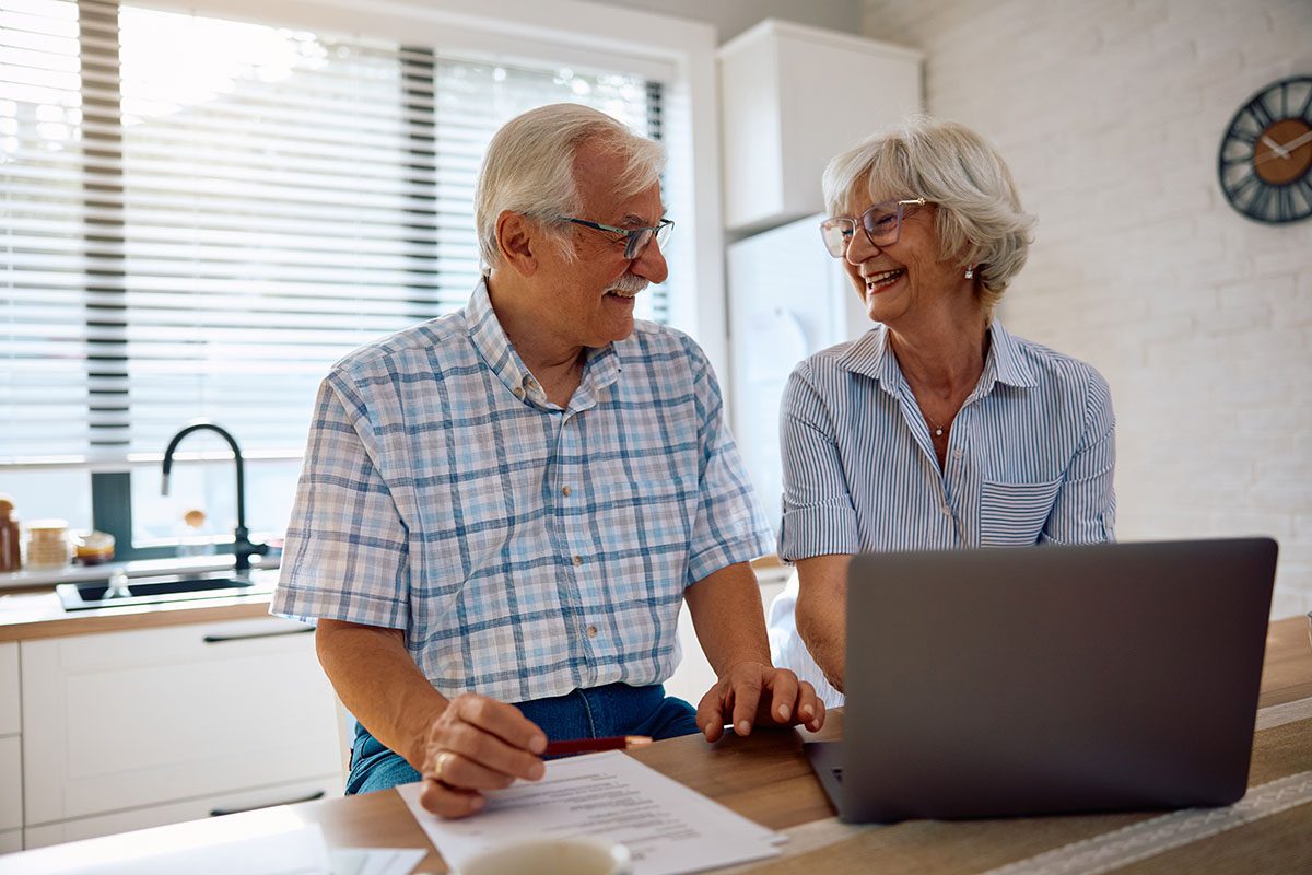 A couple sitting at their kitchen table at home, looking over financial paperwork together